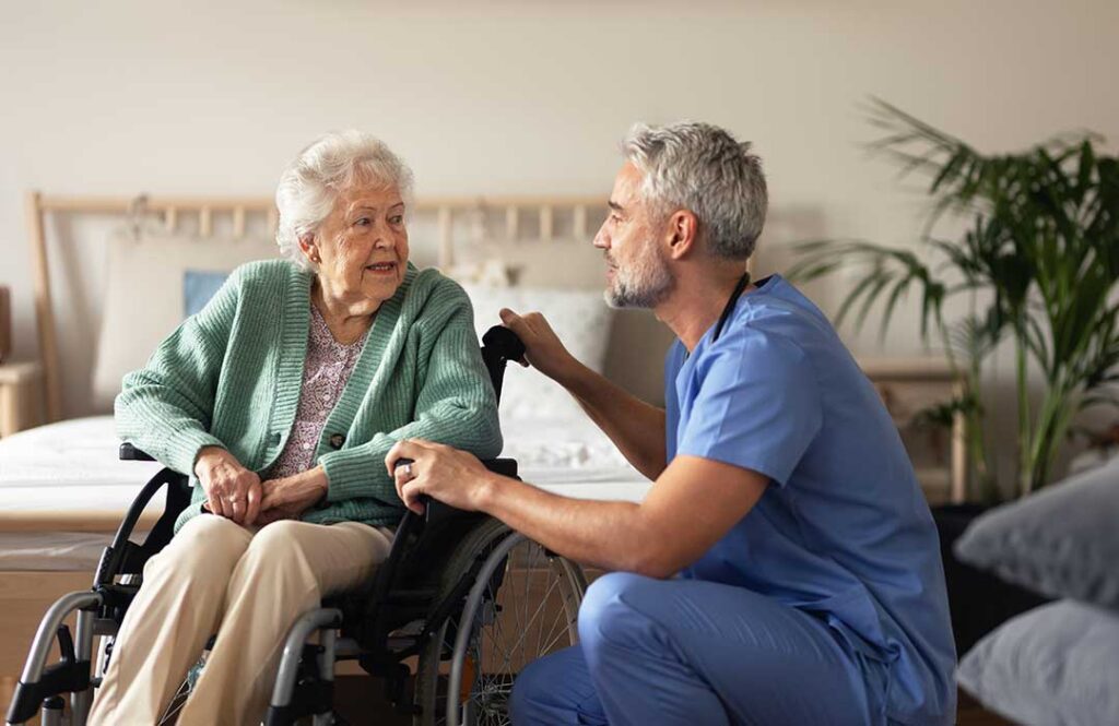 Caregiver helping an older resident walk through a bright assisted living hallway.